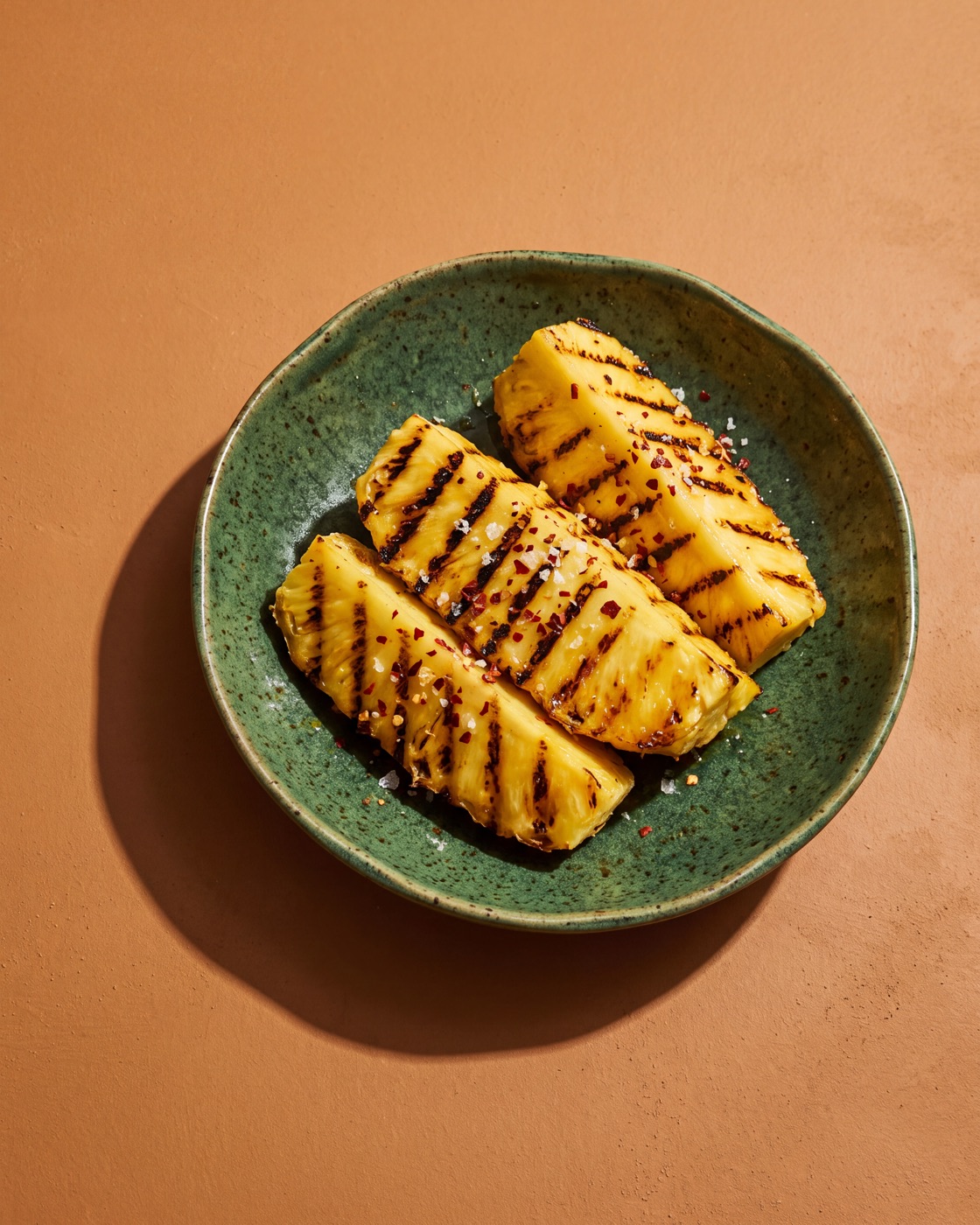 Thick pineapple wedges with black griddle stripes, scattered with chilli flakes and flaky salt