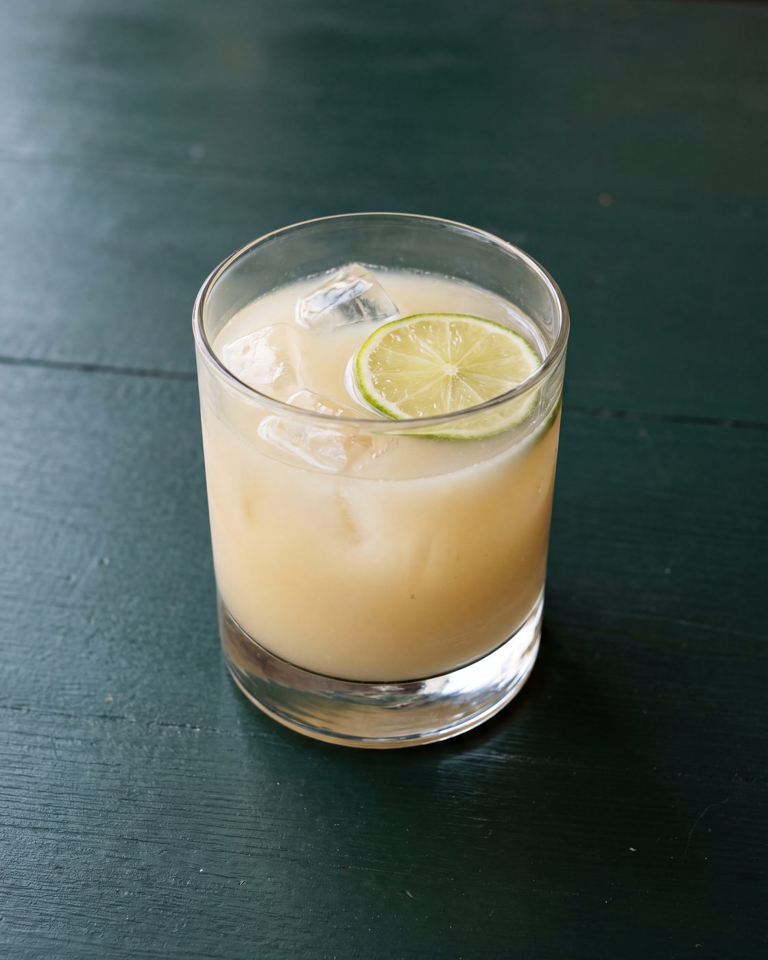 A short tumbler of pale cloudy iced ginger welcome drink with a slice of lime