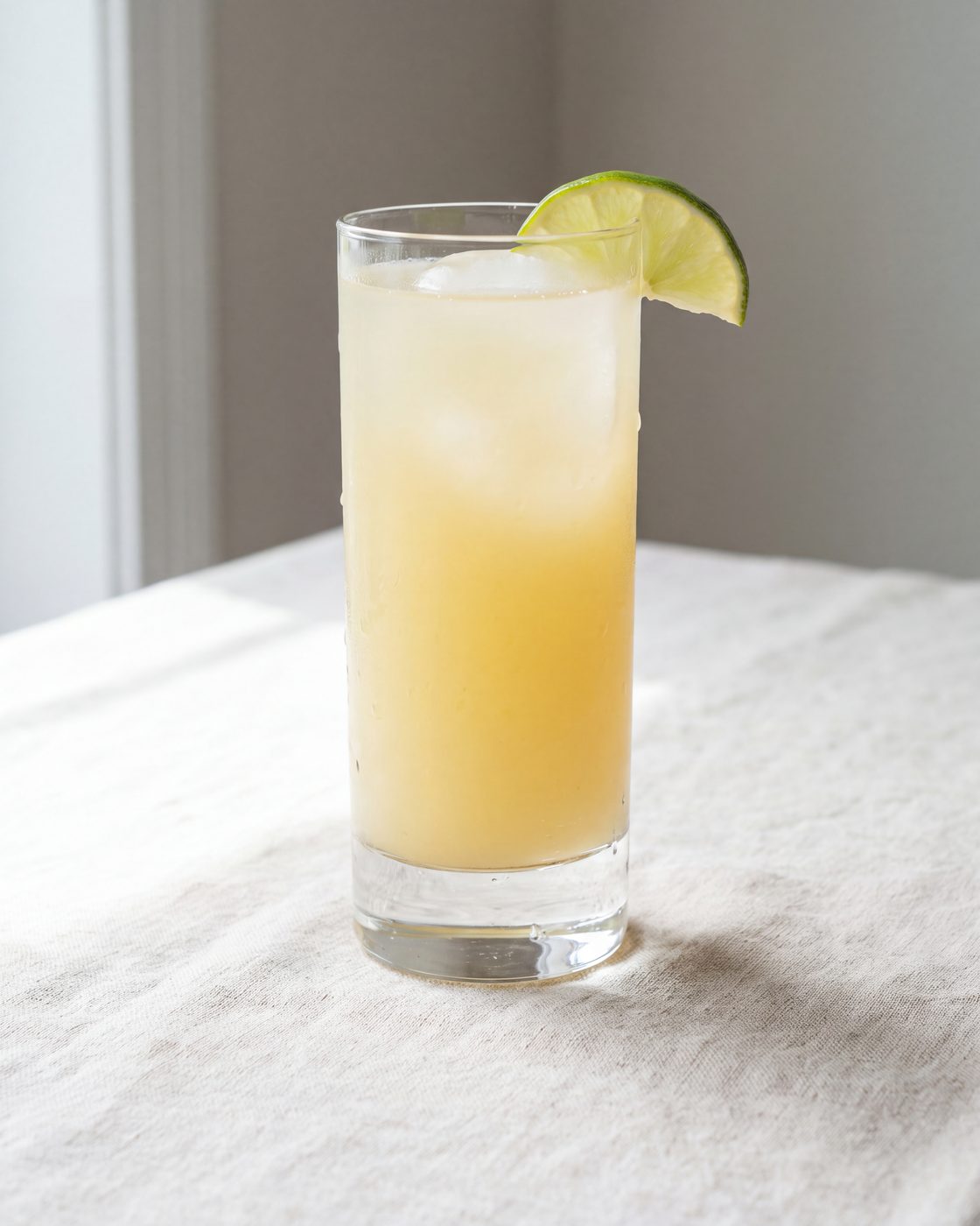 A tall glass of cloudy kink ginger soda over ice with a lime wedge