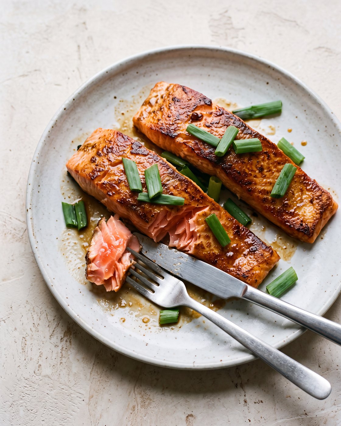 A forkful of kink glazed salmon lifted from the fillet, moist pink flesh under charred skin and a cloudy ginger glaze