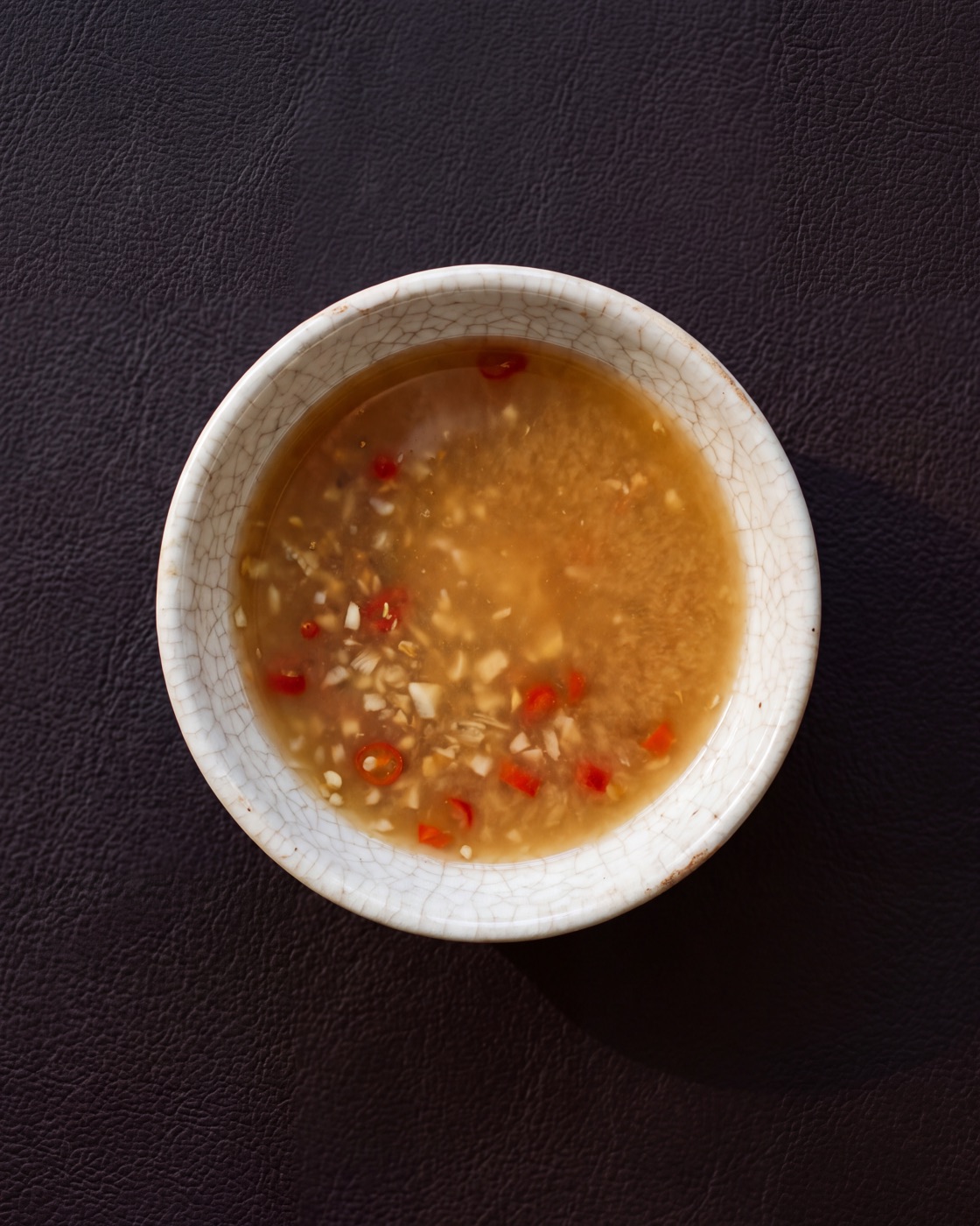 A cloudy amber ginger dipping sauce flecked with chilli and garlic, in a small crackle-glazed bowl
