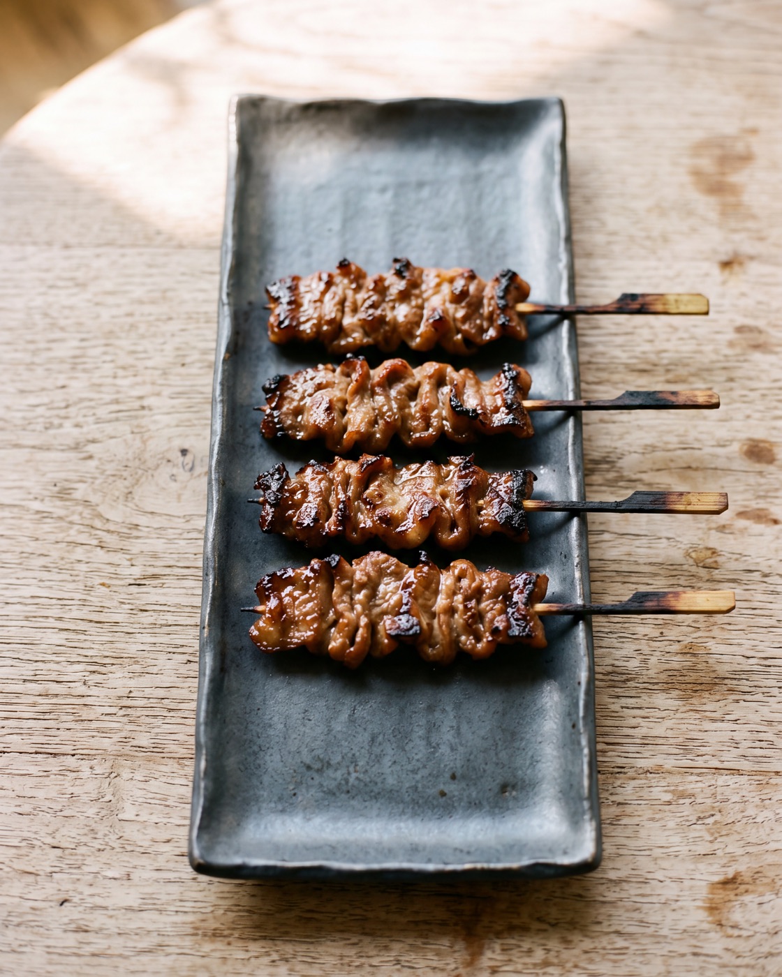 Charred sticky pork skewers on a long charcoal stoneware plate