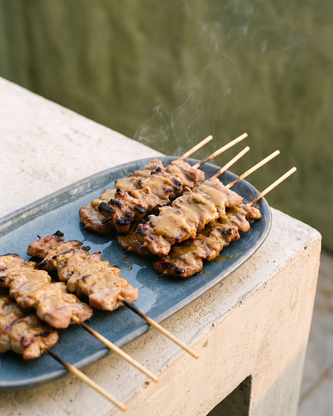 Charred sticky pork skewers on a long charcoal stoneware plate